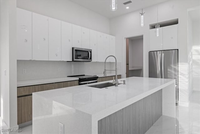 kitchen featuring decorative light fixtures, stainless steel appliances, white cabinets, and a center island with sink