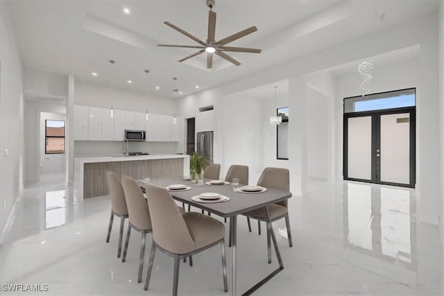 dining room with french doors, a raised ceiling, and ceiling fan with notable chandelier