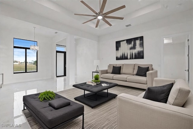 living room with ceiling fan with notable chandelier and a tray ceiling