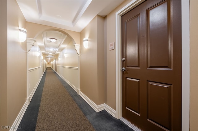 hallway with dark colored carpet and a tray ceiling