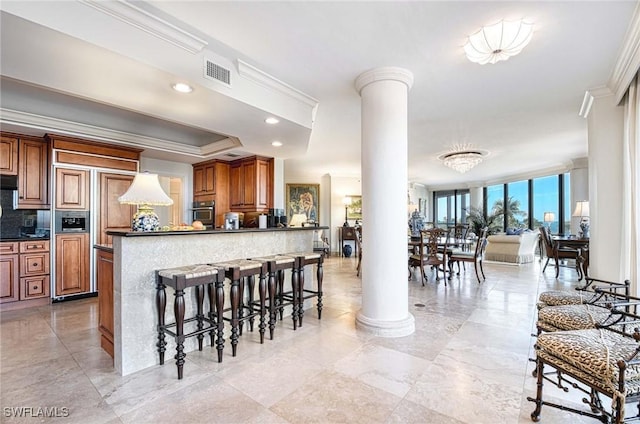 kitchen with floor to ceiling windows, ornamental molding, a kitchen bar, and decorative columns