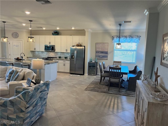 kitchen with appliances with stainless steel finishes, white cabinetry, pendant lighting, an island with sink, and light tile patterned flooring