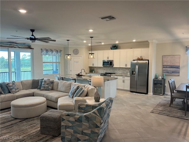 living room featuring ceiling fan, sink, light tile patterned flooring, decorative columns, and crown molding