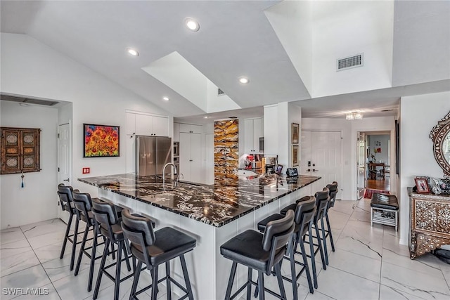 kitchen with white cabinetry, vaulted ceiling, dark stone countertops, kitchen peninsula, and stainless steel fridge