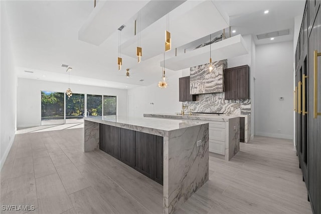 kitchen with white cabinetry, light stone counters, pendant lighting, a spacious island, and dark brown cabinets