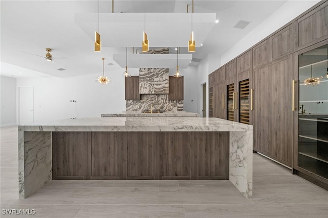 kitchen with decorative backsplash, light stone counters, dark brown cabinetry, ceiling fan, and hanging light fixtures