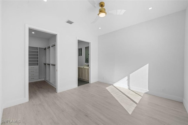 unfurnished bedroom with ensuite bath, ceiling fan, light hardwood / wood-style flooring, a spacious closet, and a closet