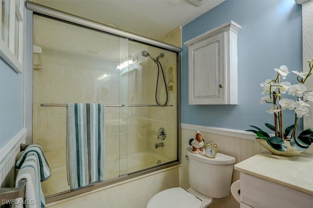 full bathroom featuring wood walls, shower / bath combination with glass door, vanity, and toilet