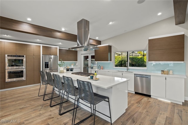 kitchen with island exhaust hood, stainless steel appliances, a breakfast bar, a spacious island, and sink