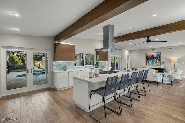 kitchen with beamed ceiling, white cabinets, french doors, and island range hood