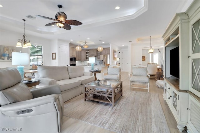 living room with ceiling fan with notable chandelier, a raised ceiling, crown molding, and light hardwood / wood-style flooring