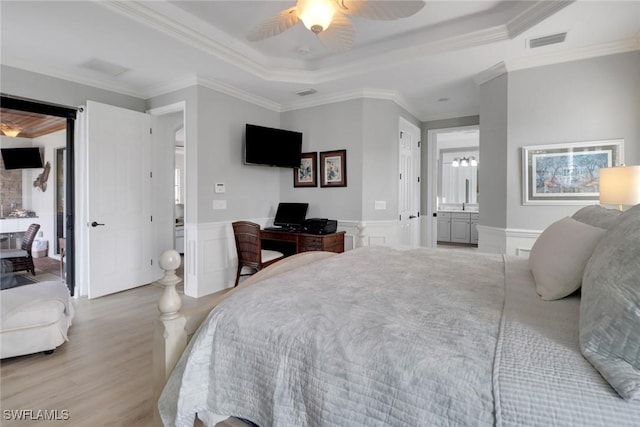 bedroom featuring light hardwood / wood-style flooring, connected bathroom, ceiling fan, a tray ceiling, and ornamental molding