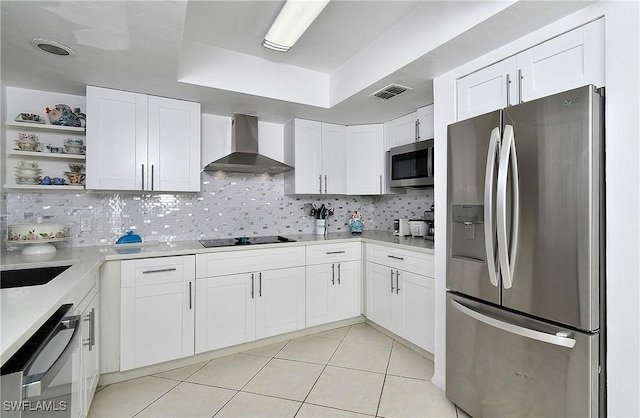 kitchen featuring wall chimney exhaust hood, white cabinetry, stainless steel appliances, decorative backsplash, and light tile patterned floors