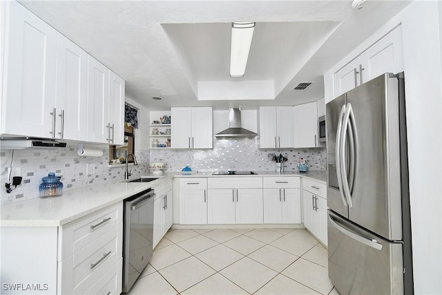 kitchen featuring appliances with stainless steel finishes, wall chimney exhaust hood, white cabinetry, sink, and a raised ceiling