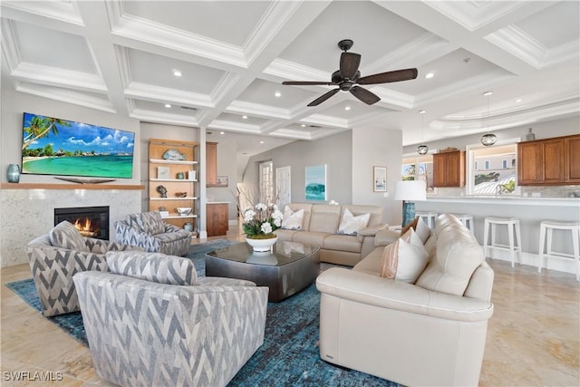 living room with coffered ceiling, ceiling fan, a premium fireplace, ornamental molding, and beam ceiling