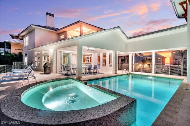 back house at dusk featuring a swimming pool with hot tub and a patio area