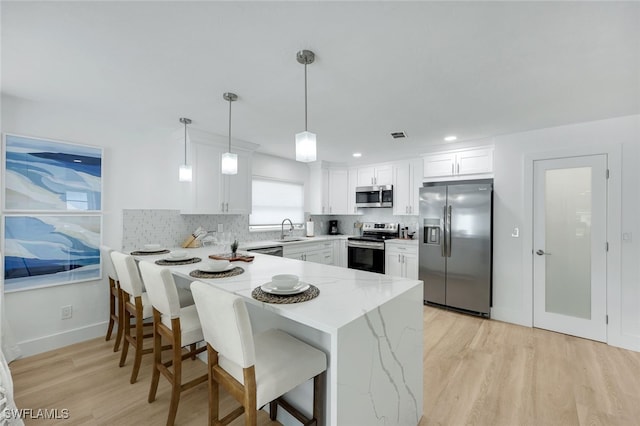 kitchen with white cabinetry, stainless steel appliances, sink, hanging light fixtures, and light stone counters