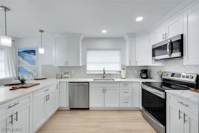 kitchen with hanging light fixtures, appliances with stainless steel finishes, sink, white cabinets, and light stone counters