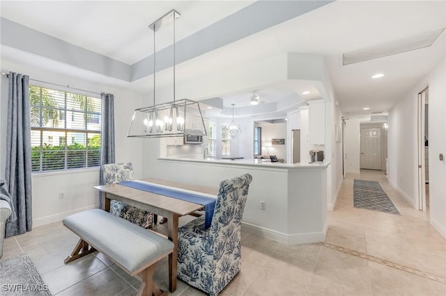 dining space featuring light tile patterned flooring, a raised ceiling, and baseboards