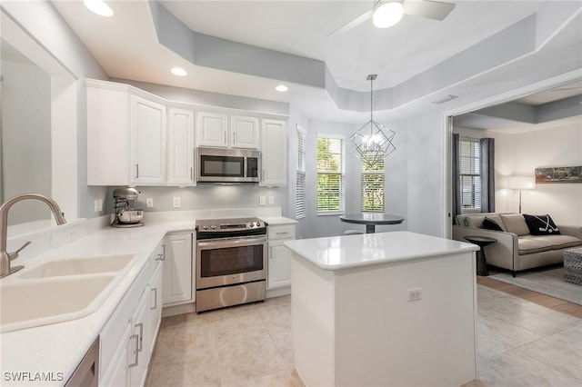 kitchen with a sink, white cabinets, appliances with stainless steel finishes, a center island, and a tray ceiling