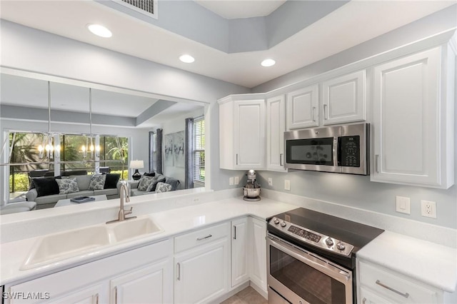 kitchen featuring a chandelier, a sink, white cabinetry, open floor plan, and appliances with stainless steel finishes