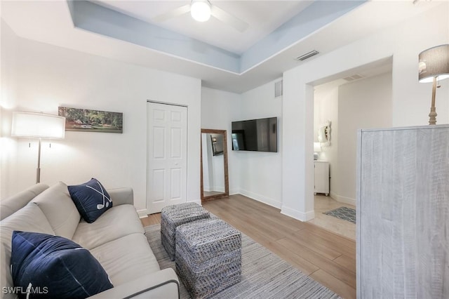 living area featuring wood finished floors, visible vents, a ceiling fan, baseboards, and a raised ceiling