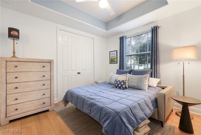 bedroom featuring light wood-style floors, a tray ceiling, a closet, and baseboards