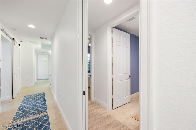 hall with a barn door, visible vents, and baseboards