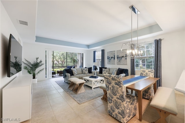 living area with a wealth of natural light, a tray ceiling, a chandelier, and visible vents