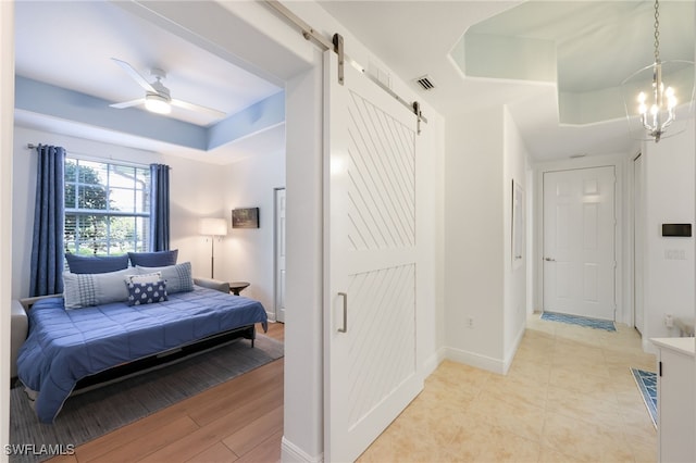 bedroom featuring a barn door, a notable chandelier, visible vents, baseboards, and a tray ceiling