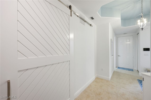 hallway featuring visible vents, a barn door, light tile patterned flooring, a chandelier, and baseboards