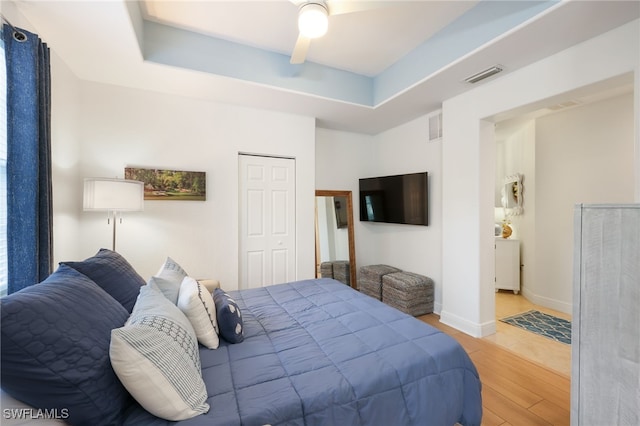 bedroom featuring a tray ceiling, wood finished floors, visible vents, and baseboards