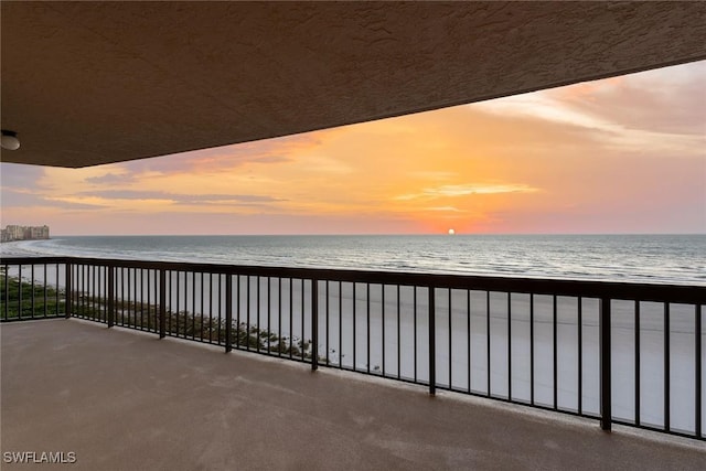 balcony at dusk with a water view and a view of the beach