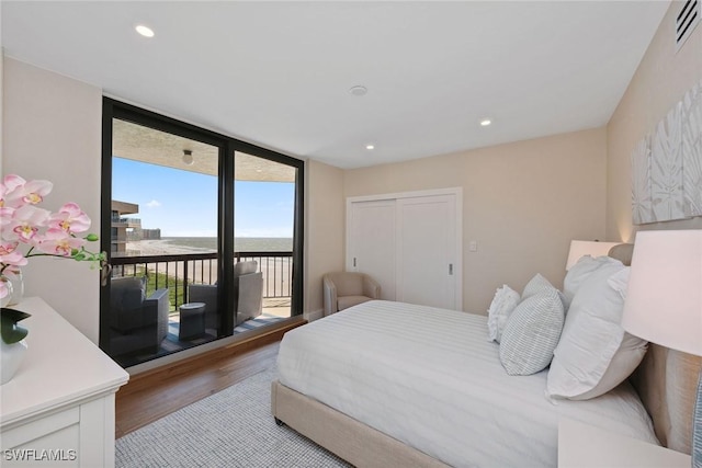 bedroom featuring expansive windows, access to outside, a water view, light hardwood / wood-style flooring, and a closet