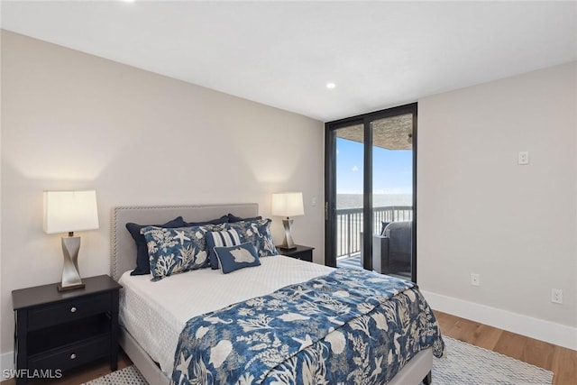 bedroom featuring hardwood / wood-style floors, a water view, a wall of windows, and access to outside