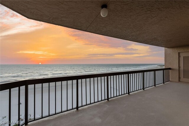 balcony at dusk featuring a water view and a view of the beach