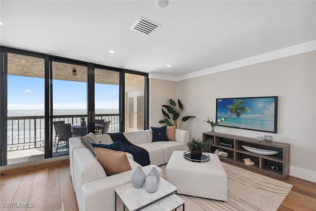 living room featuring light hardwood / wood-style flooring, a water view, ornamental molding, and a wall of windows