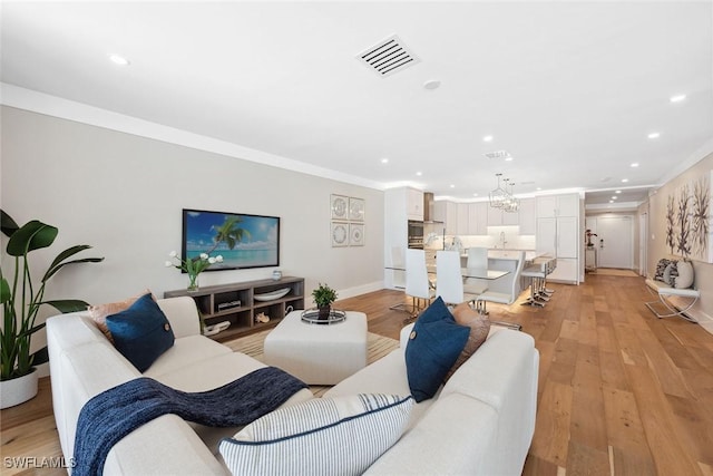 living room featuring crown molding, light hardwood / wood-style floors, and an inviting chandelier