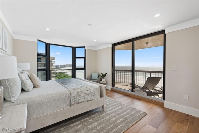 bedroom with access to exterior, hardwood / wood-style floors, a water view, and a wall of windows