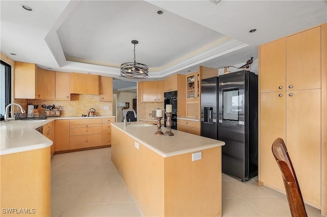 kitchen featuring pendant lighting, a raised ceiling, black appliances, a kitchen island with sink, and sink