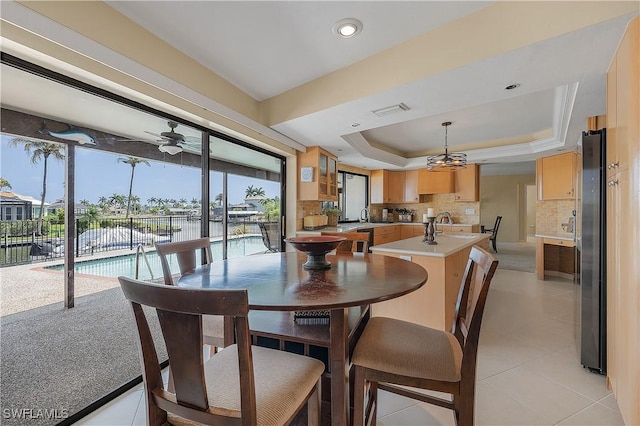 dining area featuring ceiling fan, light tile patterned floors, a water view, and a tray ceiling