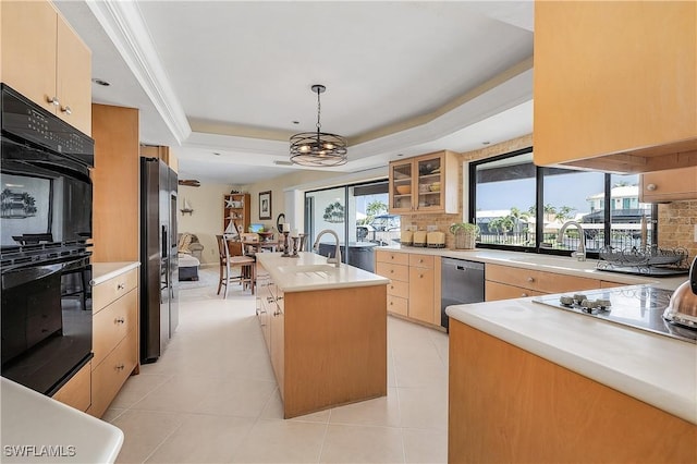 kitchen featuring a raised ceiling, a center island with sink, stainless steel appliances, light brown cabinets, and decorative light fixtures