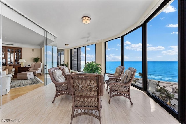 sunroom with ceiling fan, a water view, and a beach view