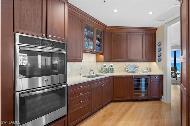 kitchen with backsplash, sink, light hardwood / wood-style flooring, stainless steel double oven, and beverage cooler