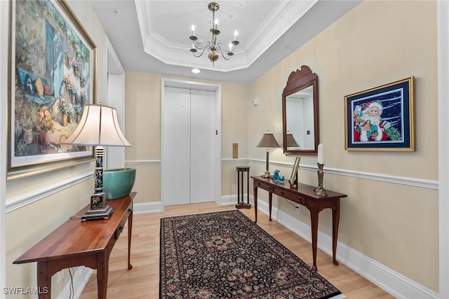 foyer with a raised ceiling, ornamental molding, light hardwood / wood-style flooring, and an inviting chandelier