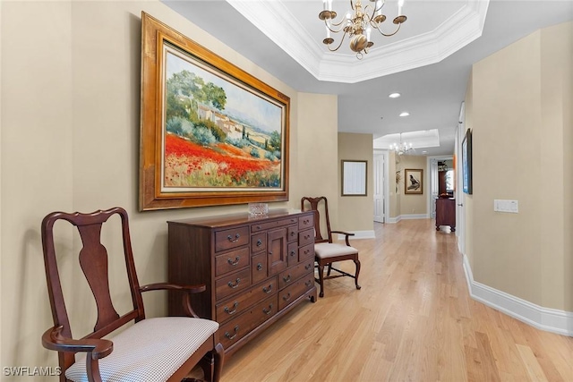 hall with a tray ceiling, crown molding, light wood-type flooring, and an inviting chandelier