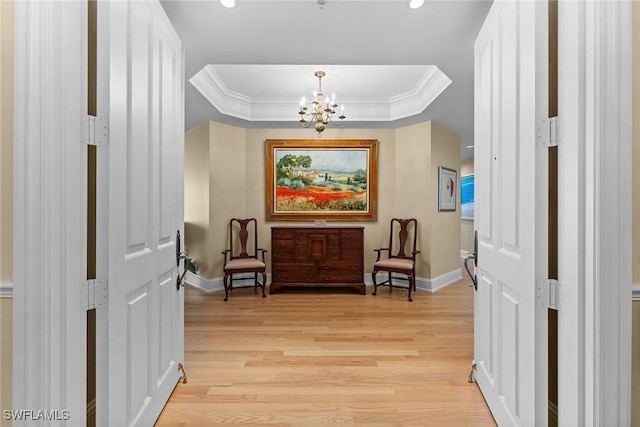 living area featuring baseboards, a tray ceiling, a chandelier, ornamental molding, and light wood-style floors