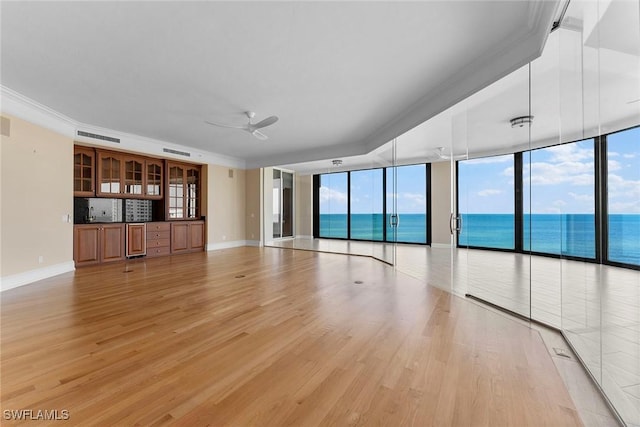 unfurnished living room with light wood-style floors, baseboards, ceiling fan, a wall of windows, and crown molding
