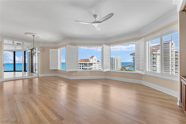 empty room with a ceiling fan, light wood finished floors, ornamental molding, baseboards, and a chandelier