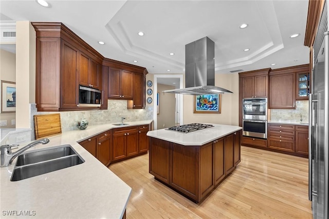 kitchen with a sink, island range hood, appliances with stainless steel finishes, a raised ceiling, and recessed lighting